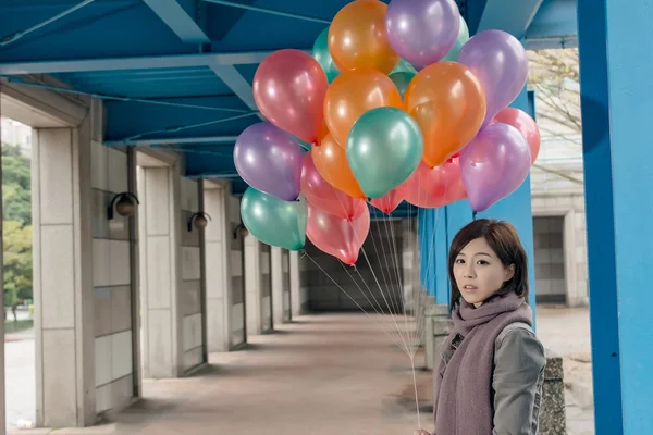 Elegant Asian beauty holding balloons under bridge — Stock Photo, Image