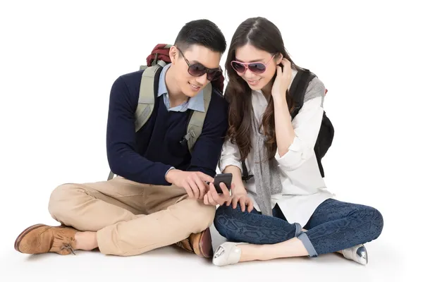 Happy traveling Asian couple sitting on ground and using cellpho — Stock Photo, Image