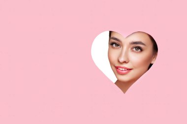 Sevgililer Günü'nün kavramsal fotoğraf. Yüz şenlikli pembe makyaj ile kızın. Pembe bir arka plan üzerinde kağıt kalpler. Aşk sembolleri Sevgililer günü