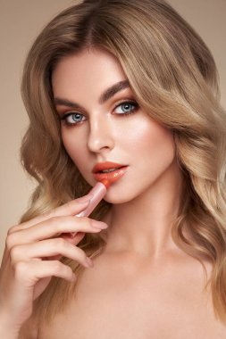 Güzel sarışın bir kadın ruj sürüyor. Sağlıklı ciltli bir model, yakın portre. Kozmetik, güzellik ve kaplıca