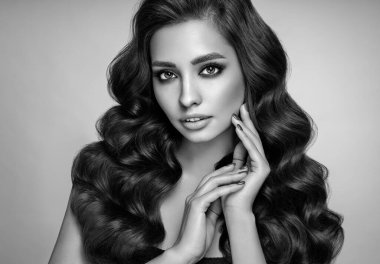 Mükemmel makyajlı esmer kız. Uzun kıvırcık saçlı, gülümseyen güzel model kadın. Bakım ve güzellik ürünleri. Siyah beyaz fotoğraf