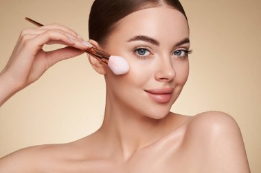 Temiz tenli güzel bir genç kadın portresi. Makyaj fırçası olan bir model. Kozmetik, güzellik ve kaplıca