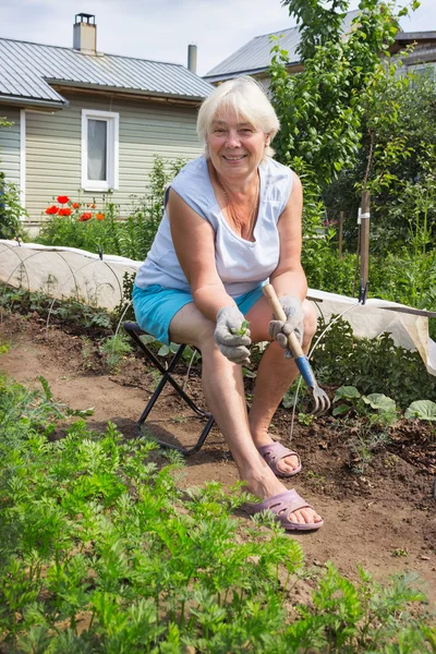 Mujer mayor elimina las malas hierbas en el jardín — Foto de Stock