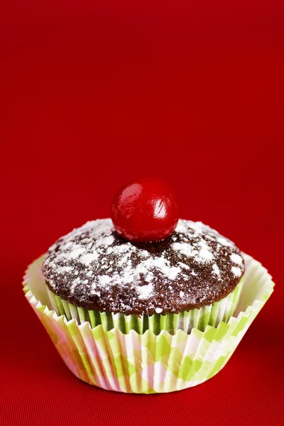 Um cupcake de chocolate com cereja sobre vermelho — Fotografia de Stock
