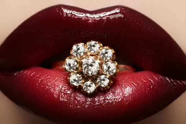 Close-up van mooie vrouw lippen met heldere mode donker rode glanzende make-up. Macro lipgloss cherry make-up. Mond met bruiloft gold diamond ring — Stockfoto
