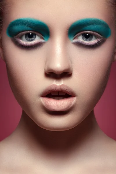 Retrato de alta moda de la expresión de la mujer joven con maquillaje de ojos de aguamarina brillante, labios llenos pálidos y piel lisa y limpia. Primer plano macro sesión de belleza sobre fondo rojo —  Fotos de Stock