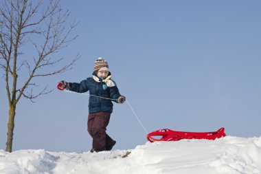 karlı bir tepe üzerinde kırmızı plastik kızak ile çocuk