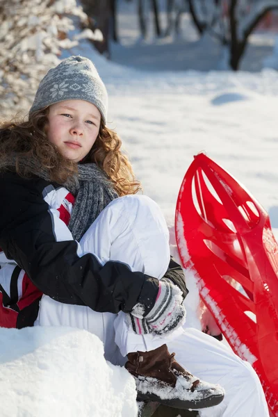 Chica con trineo de plástico rojo en un parque cubierto de nieve —  Fotos de Stock