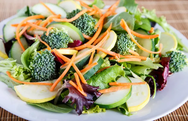 Свежий овощной салат на белой тарелке и бамбуковый мат — стоковое фото