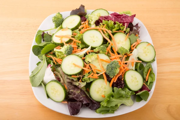 Veld groen en plantaardige salade in witte plaat op houten tafel — Stockfoto