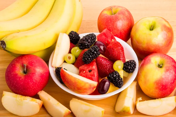 Skjær frukt i boller med bananer og hele og avskårne epler – stockfoto