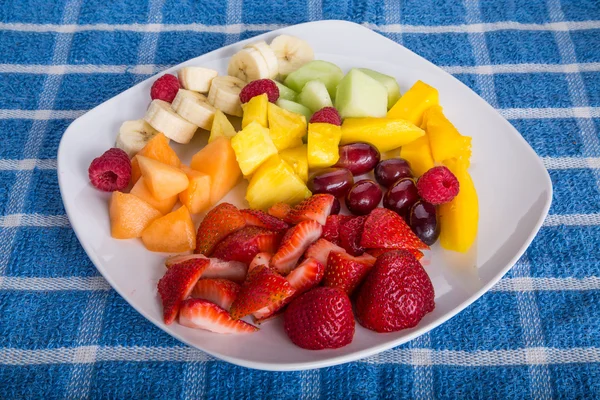 Morangos com frutas cortadas na placa branca — Fotografia de Stock