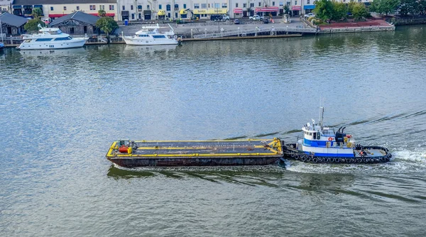 Tugboat Pushing Barge Past River Street in Savannah, Georgia — стокове фото