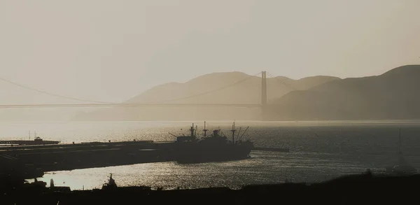 Silhouette of Industrial Ship in San Francisco with Golden Gate Bridge through fog in background
