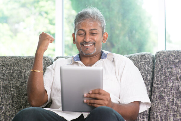 Indian man cheering while using tablet pc