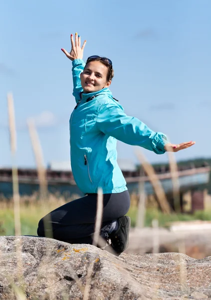 Beautiful girl in a jacket kneeling on a rock — Stock Photo, Image