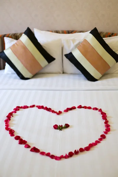 Corazón de pétalos de rosa dispuestos en la cama — Foto de Stock