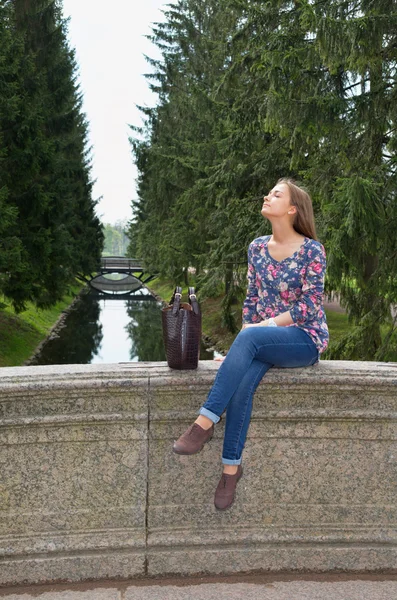 Eautiful girl sits on an old stone bridge — Stock Photo, Image