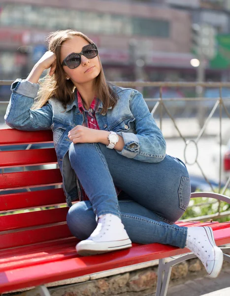 Mädchen in Jeans sitzt auf einer Bank auf der Straße — Stockfoto