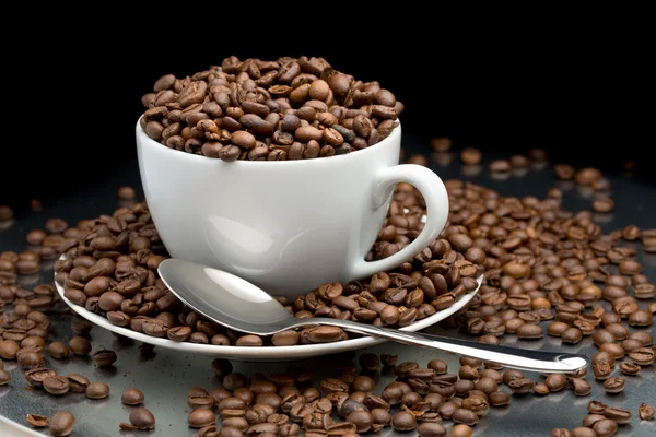 Cup and saucer full of coffee beans with a spoon — Stock Photo, Image