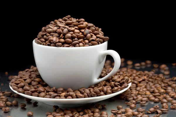 Cup and saucer full of coffee beans — Stock Photo, Image