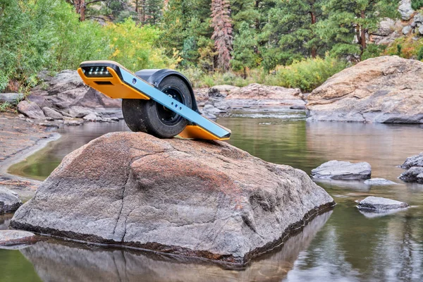 one-wheeled electric skateboard on a rocky shore of mountain river with a fall scenery