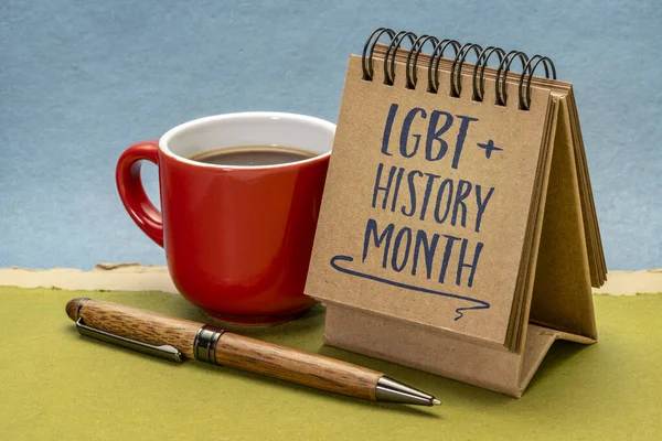 LGBT History Month - handwriting in a small desktop calendar with a cup of coffee against abstract paper landscape, reminder of cultural and heritage event