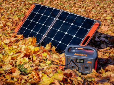Fort Collins, CO, ABD - 4 Kasım 2021: Jackery Explorer 500, 518Wh Portable Power Station, renkli kuru yapraklarla kaplı bir alanda güneş paneli tarafından şarj ediliyor..