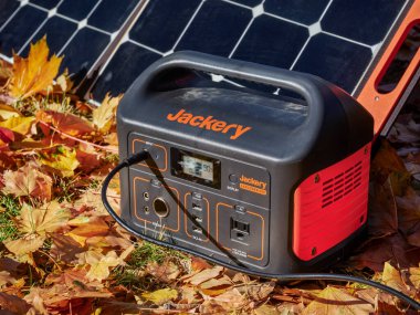 Fort Collins, CO, ABD - 4 Kasım 2021: Jackery Explorer 500, 518Wh Portable Power Station, renkli kuru yapraklarla kaplı bir alanda güneş paneli tarafından şarj ediliyor..