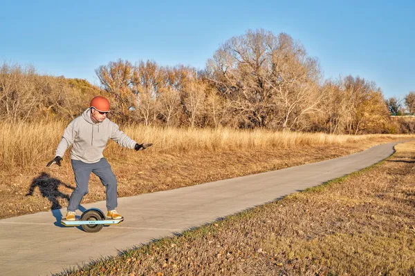 シニア マンはコロラド州の秋の風景の舗装された自転車道で電動スケートボードに乗っています — ストック写真