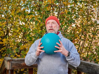 Son sınıf öğrencisi erkek (60 'lı yaşların sonlarında) arka bahçesinde serin bir öğleden sonra serin bir top ile egzersiz yapıyor.