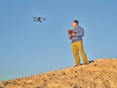 Grover, CO, USA - November 22, 2021: Senior male pilot with ipad tablet and radio controller is operating Mavic 3, an advanced, foldable consumer drone by DJI in desert area. clipart