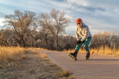 Fort Collins, Colorado 'daki Poudre Nehri boyunca asfalt bir bisiklet yolunda paten kayarken - son sınıf erkek patenci tepe freni, düşme veya kış manzarası kullanmayı bırakıyor