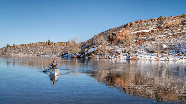 senior male wearing life jacket  is paddling expedition canoe in witer scenery of Horsetooth Reservoir in northern Colorado