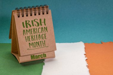 March Irish American Heritage Month - Masaüstü takviminde İrlanda bayrağı renkleriyle soyut kağıda karşı el yazısı (yeşil, beyaz ve turuncu), kültürel etkinliğin hatırlatıcısı