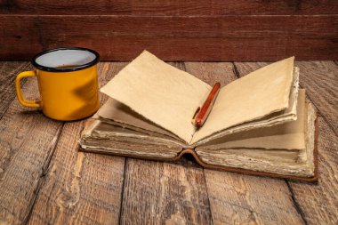 blank antique leather-bound journal with decked edge handmade paper pages with a stylish pen and cup of tea on rustic wood, journaling concept clipart
