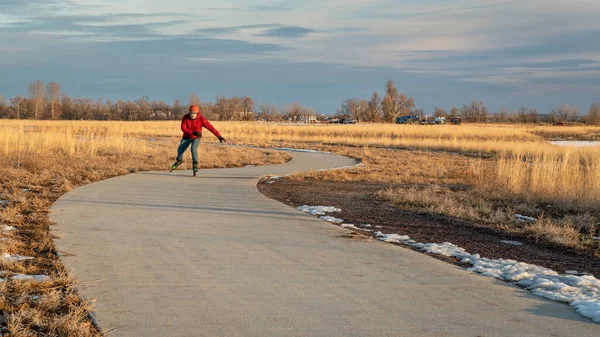 シニア男性はコロラド北部の日没秋冬の風景で舗装された自転車道でインラインスケートをしています — ストック写真