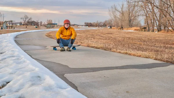 在科罗拉多州北部的博伊德湖州立公园 戴着头盔的老人正坐在一块滑板上 这是一条铺好的自行车道 是冬季的风景 — 图库照片