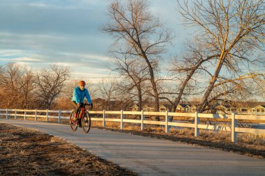 Son sınıf erkek bisikletçi, sonbaharda ya da kış mevsiminde Kuzey Colorado 'da WIndsor yakınlarındaki Poudre River Trail' de sayısız bisiklet yolundan birinde çakıl bisikleti sürüyor.