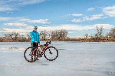Kış veya ilkbahar başında donmuş bir gölde çakıl bisikletli yaşlı bir erkek bisikletçi - Arapaho Bend Doğal Alanı Fort Collins, Colorado