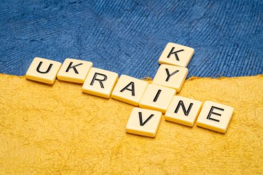 Fildişi harflerle Ukrayna ve Kyiv bulmacaları Ukrayna ulusal bayrağının mavi ve sarı renkleriyle soyut kağıt parçalarına karşı.