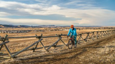 Son sınıf erkek bisikletçi, Fort Collins, Colorado 'daki Rocky Dağları' nın etekleri ve ön sıradağları manzaralı çamurlu bir patikada çakıl bisikleti sürüyor.