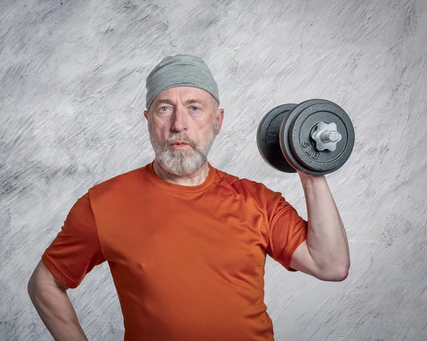 casual portrait of old bearded  man (in late 60s) exercising with heavy dumbbells, active senior and fitness concept