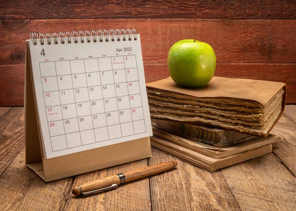 2022年4月 带有旧书 旧杂志和苹果的螺旋式桌面日历 与乡村谷仓木料背景 时间和商业概念相抗衡 — 图库照片