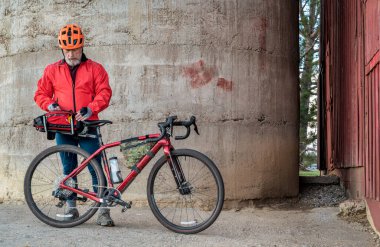 Colorado 'nun kırsal kesimindeki eski ahırda mola veren çakıllı bisikletli yaşlı bir erkek bisikletçi.