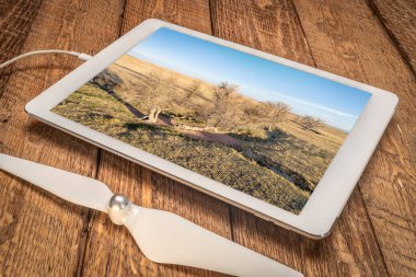 İlkbaharın başlarında Colorado ovasında bir dere boyunca uzanan ağaçlar dijital tabletteki bir hava görüntüsünü inceliyor.