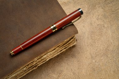 antique leather-bound journal or book with decked edge handmade paper pages and a stylish pen on a handmade bark paper, journaling concept clipart