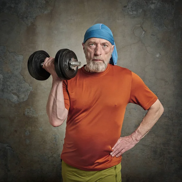 casual portrait of old bearded  man (in late 60s) exercising with heavy dumbbell, active senior and fitness concept, grunge urban background