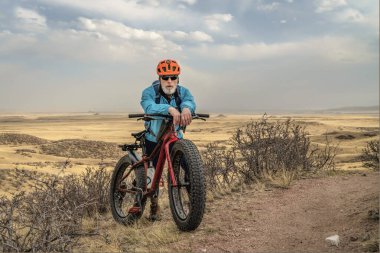 Kuzey Colorado otlağında tek bir patika üzerinde şişman bir dağ bisikleti olan yaşlı bir erkek bisikletçi. İlkbahar başlarında Fort Collins yakınlarındaki Soapstone bozkırında doğal manzara.