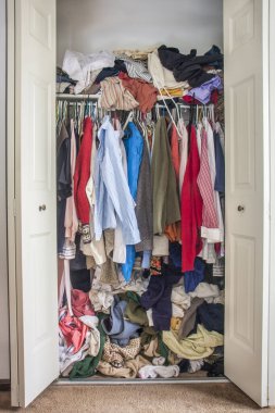 messy closet overfilled with colorful woman clothes on hangers and stuffed in any available space, need for declutter concept
